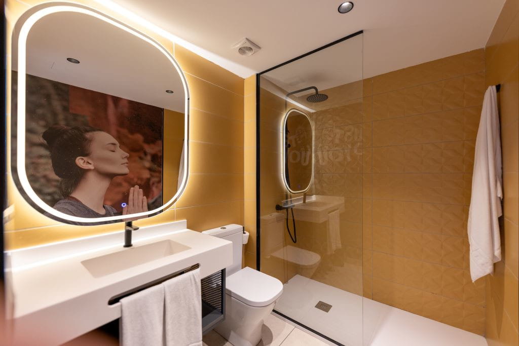 Badezimmer mit Dusche, Waschbecken, beleuchtetem Spiegel und Foto einer Frau beim Meditieren auf Teneriffa.