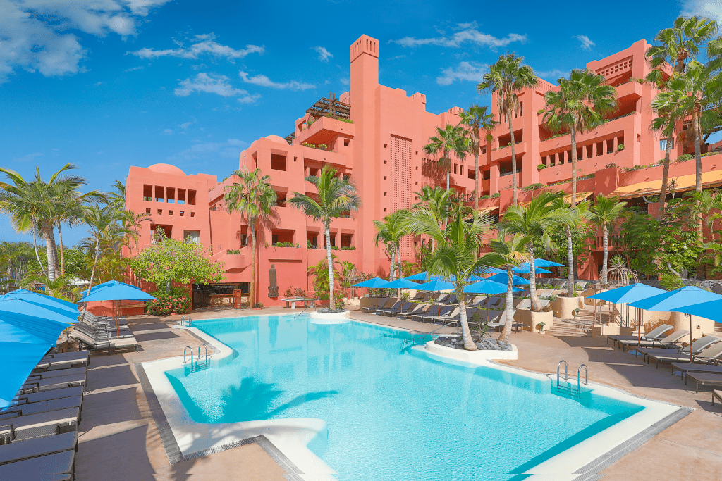 Rotes Hotelgebäude mit Pool und blauen Sonnenschirmen in Tenerife.
