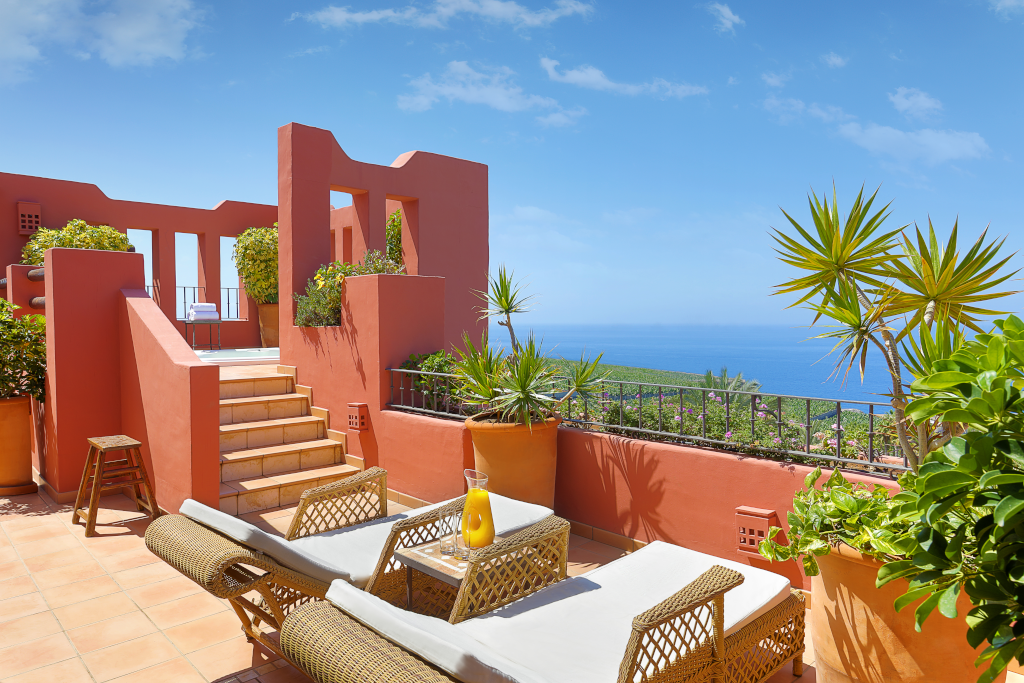 Terrasse mit Meerblick in Teneriffa, umgeben von Pflanzen und Liegestühlen.