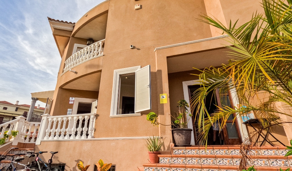 Fassade eines Hauses in Costa Adeje, Teneriffa, mit Palmen und Fahrrädern.