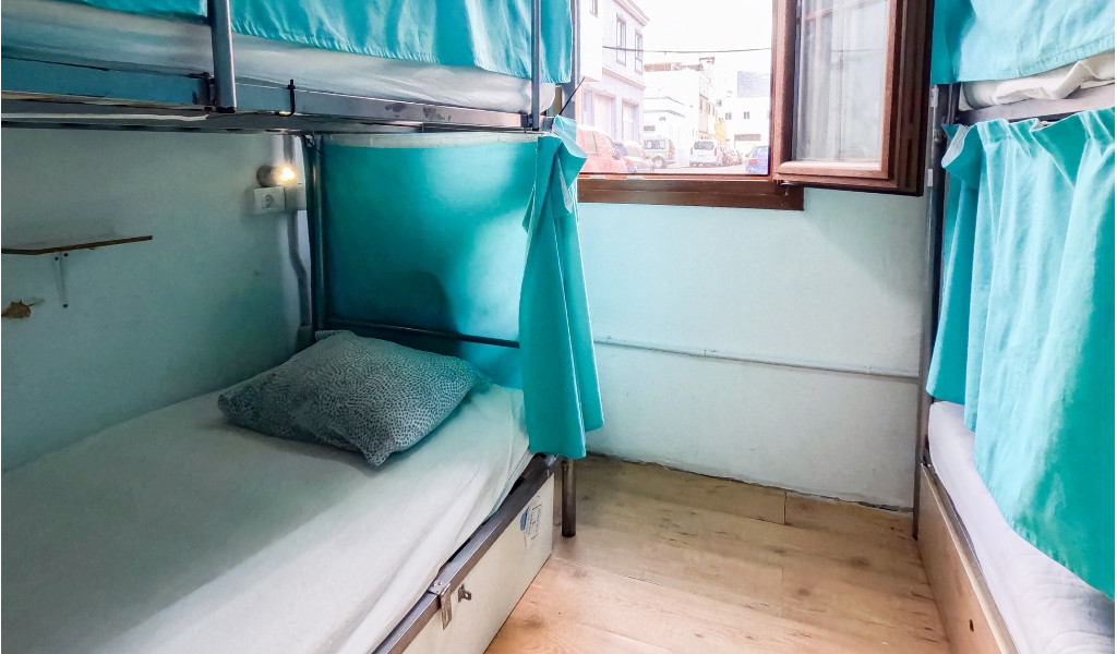 Stockbett mit türkisfarbenen Vorhängen und Fensterblick in einem Hostel in Puerto de la Cruz.