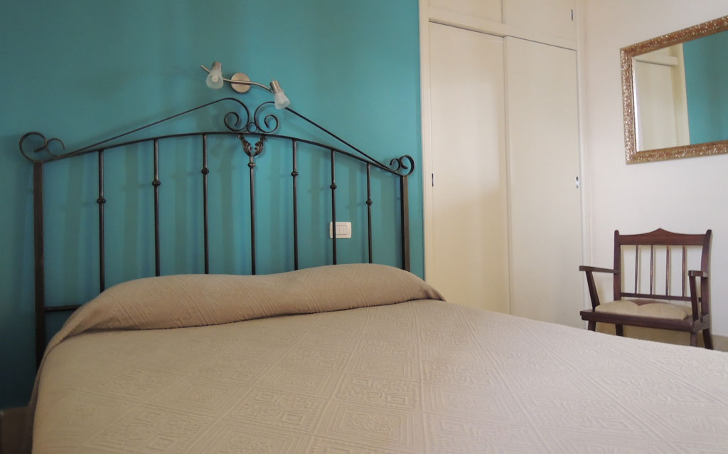 Schlafzimmer mit Metallbett, blauer Wand, Stuhl und Spiegel in Santa Cruz, Teneriffa.
