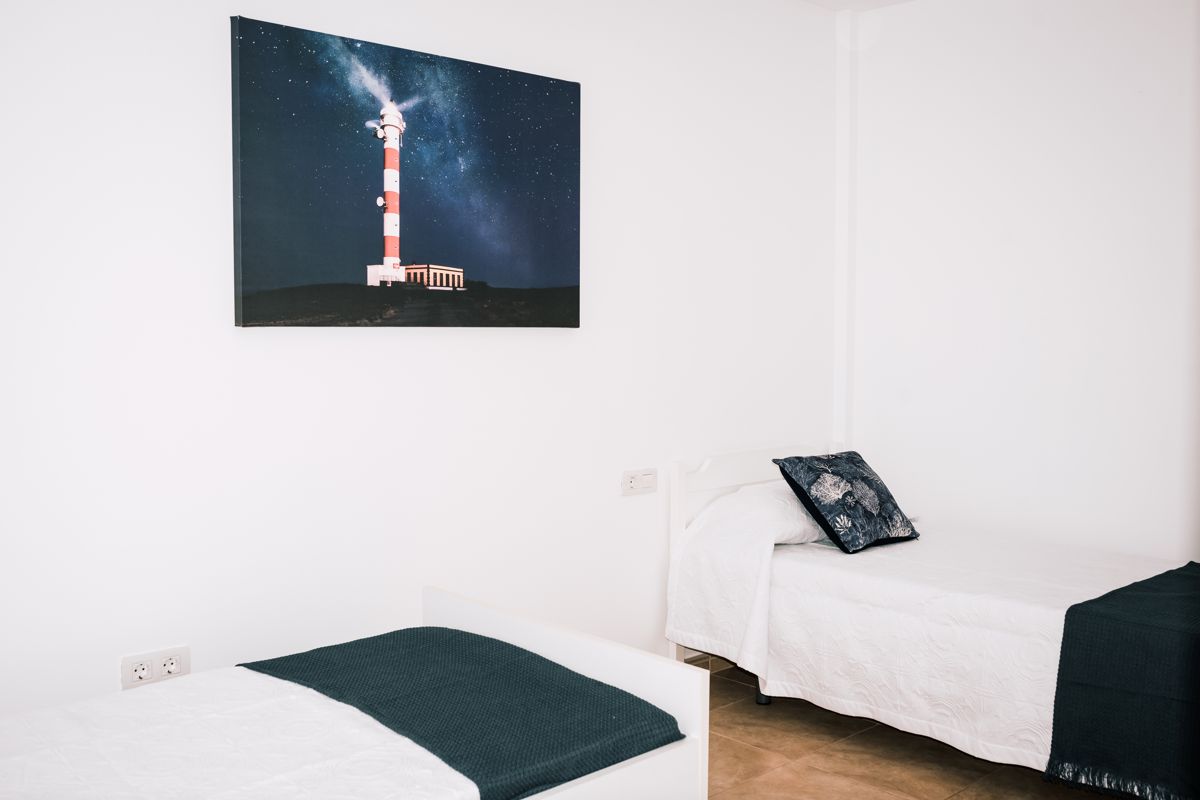 Zwei Betten in einem Zimmer mit einem Bild eines Leuchtturms von Teneriffa an der Wand.