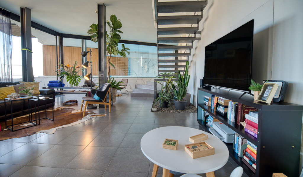 Offenes Wohnzimmer mit Treppe, Pflanzen, Bücherregal und großem Fernseher in Teneriffa.