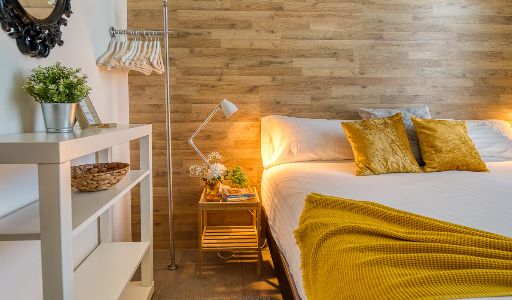 Bett mit gelben Kissen und Decke, Holzwand in einem Zimmer in Teneriffa.