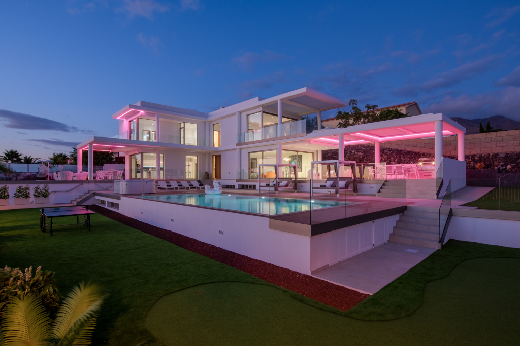 Moderne Villa mit Pool und beleuchteter Terrasse in Costa Adeje, Teneriffa bei Abenddämmerung.