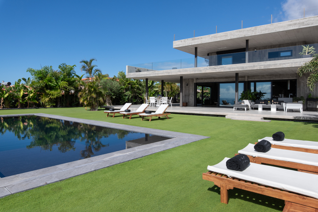 Moderne Villa mit Pool und Liegestühlen in Teneriffa, umgeben von üppigem Garten.