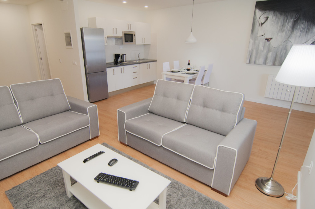 Wohnzimmer und Küche in einer Wohnung auf Teneriffa mit grauen Sofas, Tisch und Kunst.
