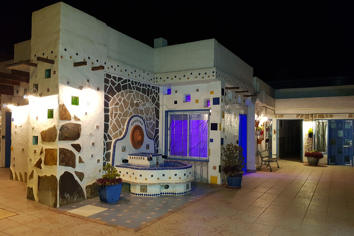 Gebäude in Sansofé, Teneriffa, bei Nacht mit beleuchteten Mosaiken und Pflanzen.