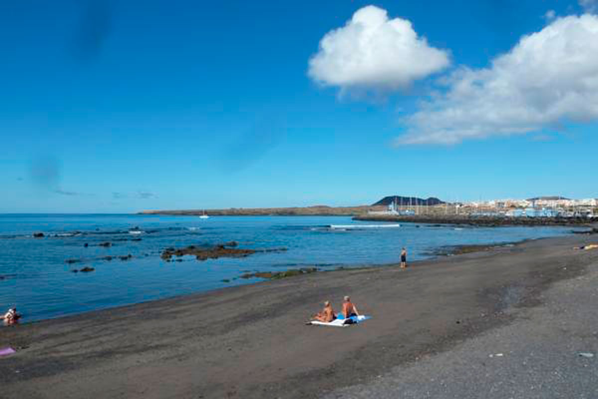 Strand in El Médano, Teneriffa mit blauem Himmel und Menschen am Ufer.