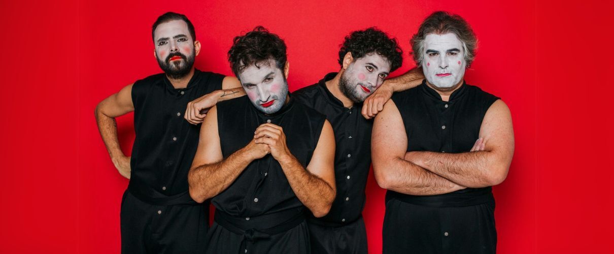 Vier Männer mit Gesichtsbemalung in schwarzer Kleidung vor rotem Hintergrund in Tenerife.