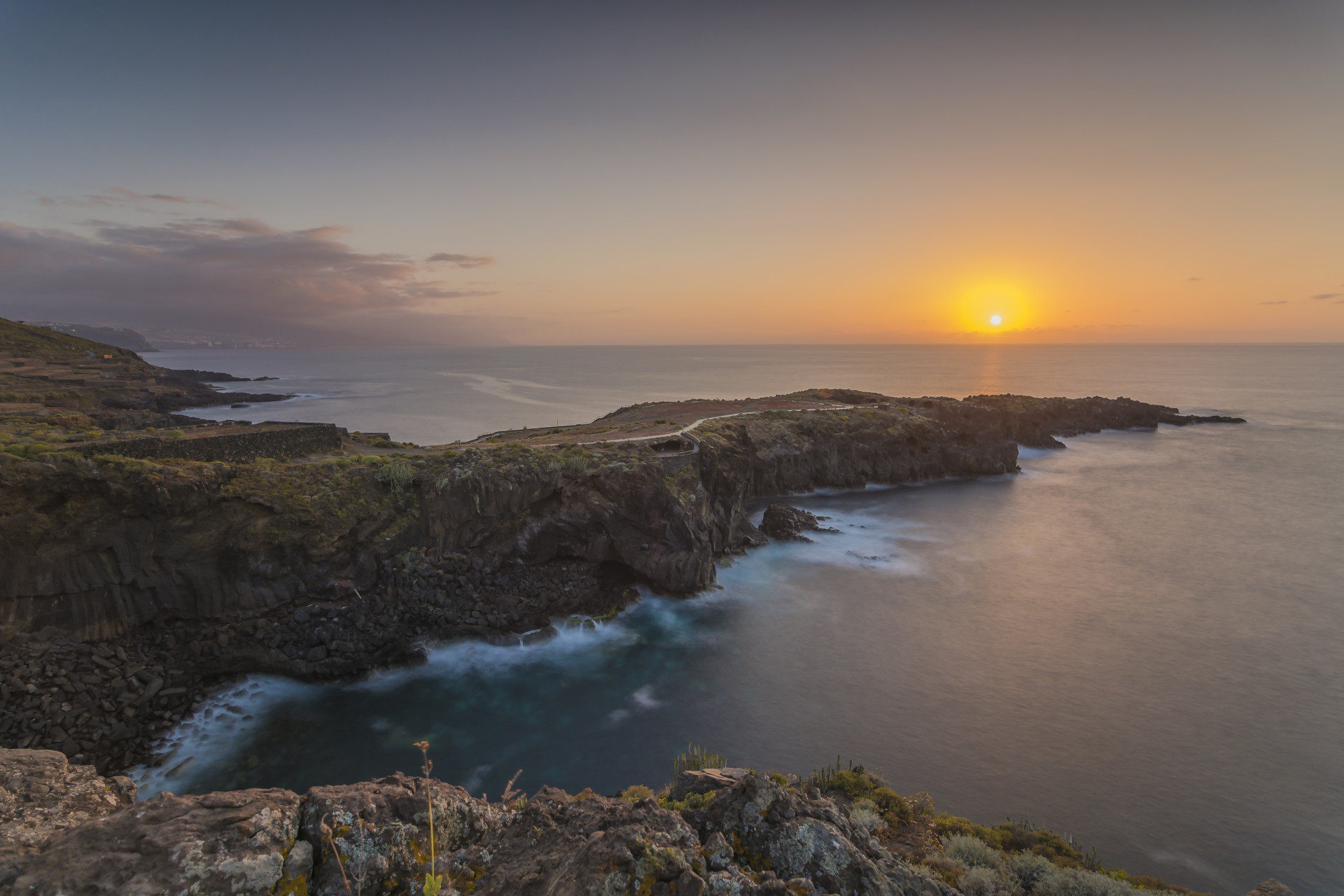 Sonnenuntergang an der Küste Teneriffas mit Klippen und Meer am Horizont.