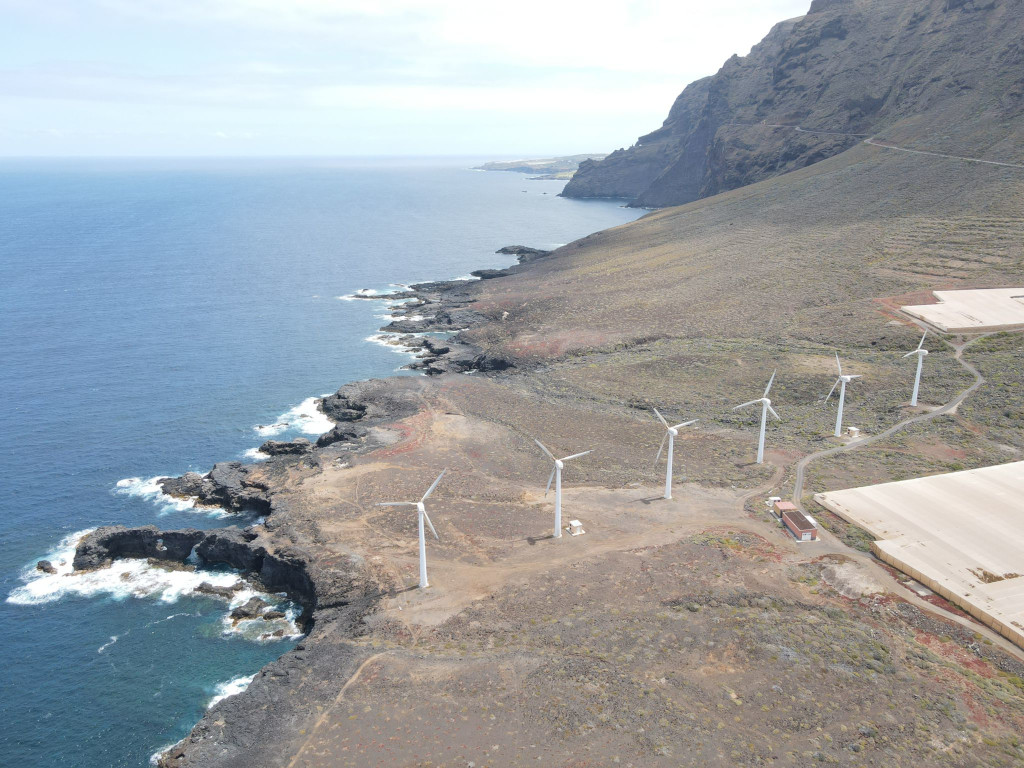 Windturbinen an der Küste Teneriffas neben Klippen und Meer.
