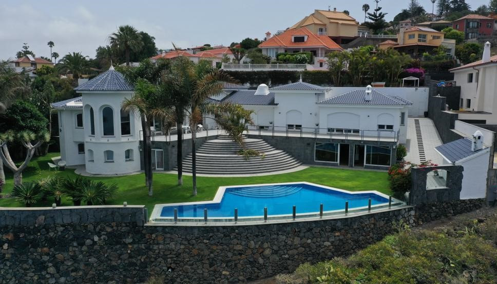 Moderne Villa mit Pool und Garten auf Teneriffa, umgeben von Häusern und Palmen.