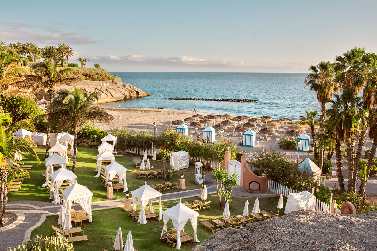 Strand mit Sonnenschirmen und Hütten in Costa Adeje, Teneriffa, bei Sonnenuntergang.