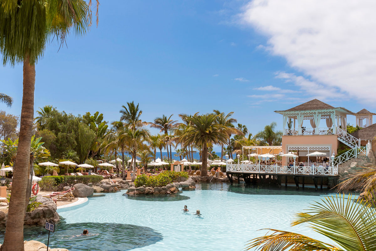 Schwimmbad, umgeben von Palmen, und ein Gebäude im Hotel auf Teneriffa.