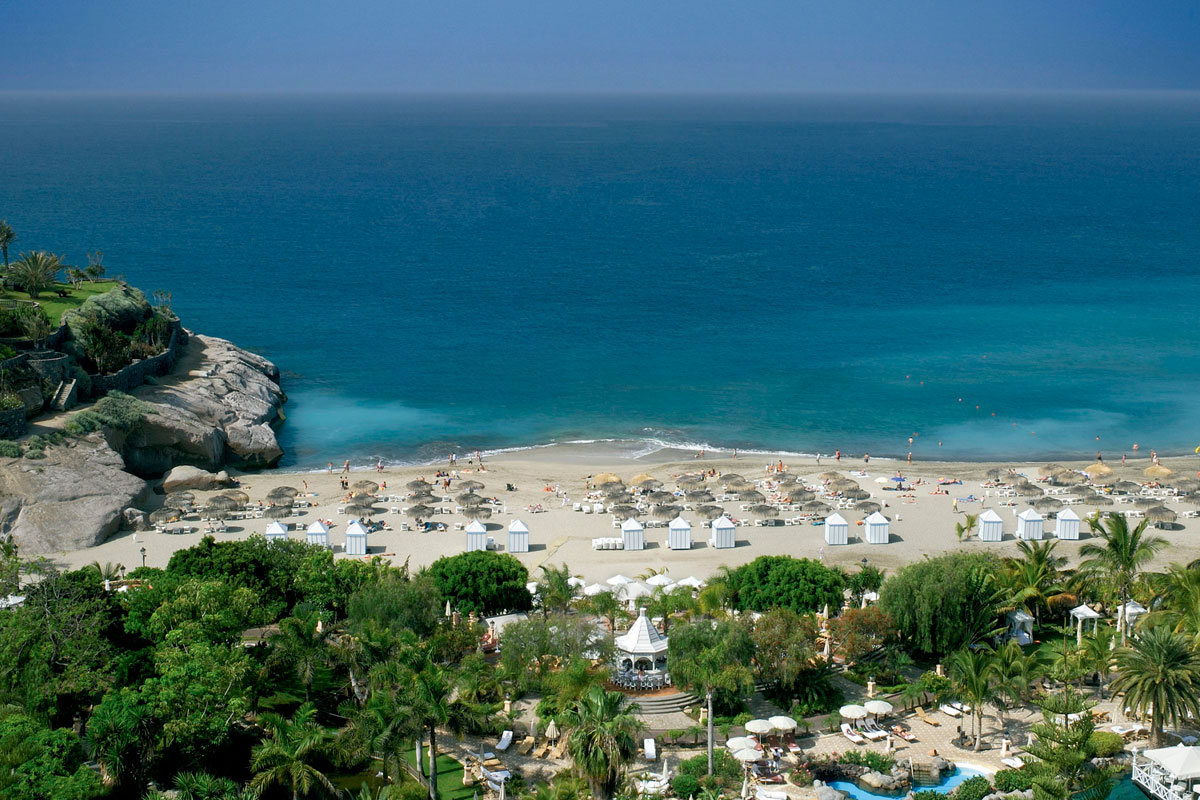 Playa del Duque auf Teneriffa mit Sonnenschirmen und Hütten am Meer.