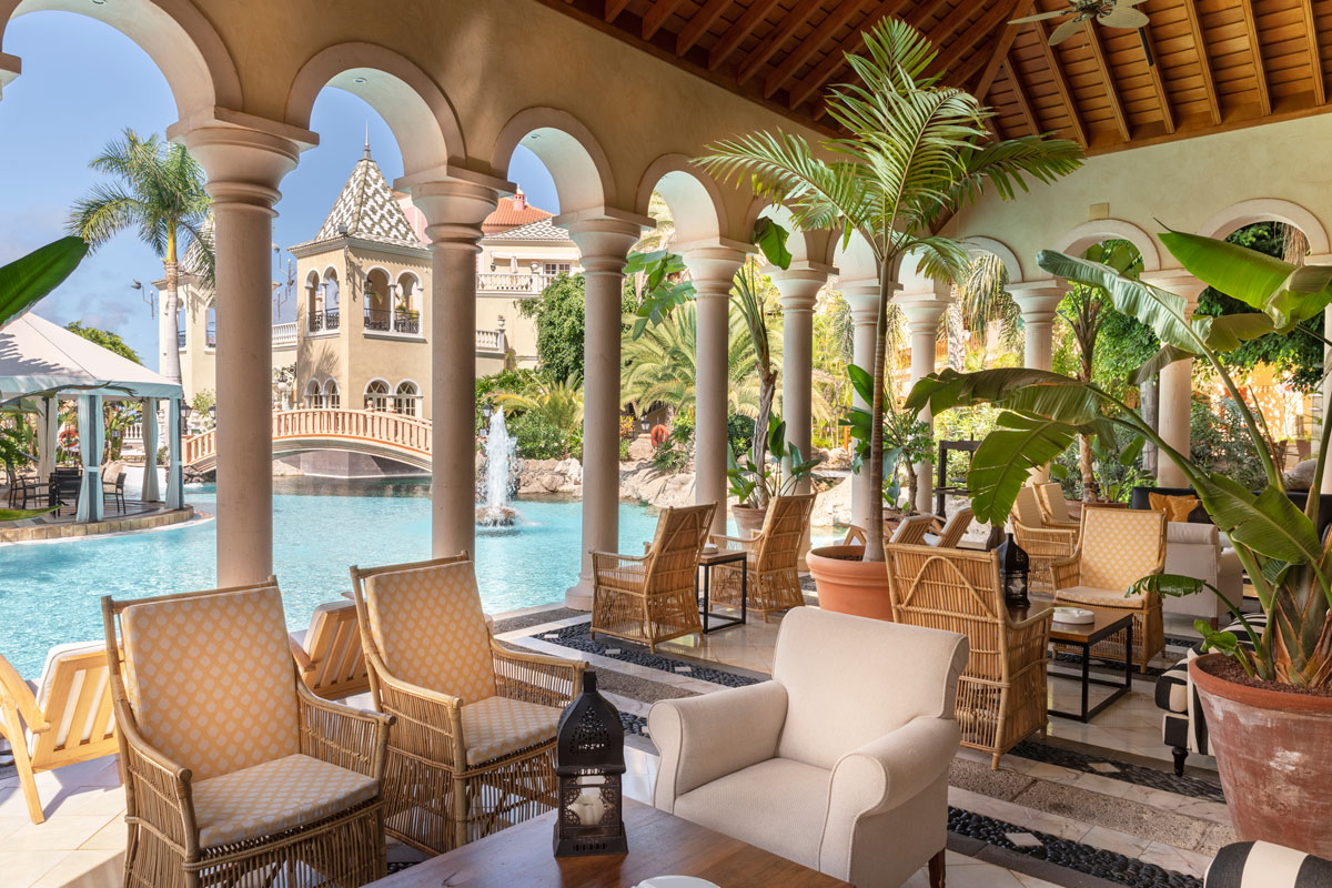 Terrasse mit Pool und Brunnen in einem Hotel auf Teneriffa, umgeben von Palmen.