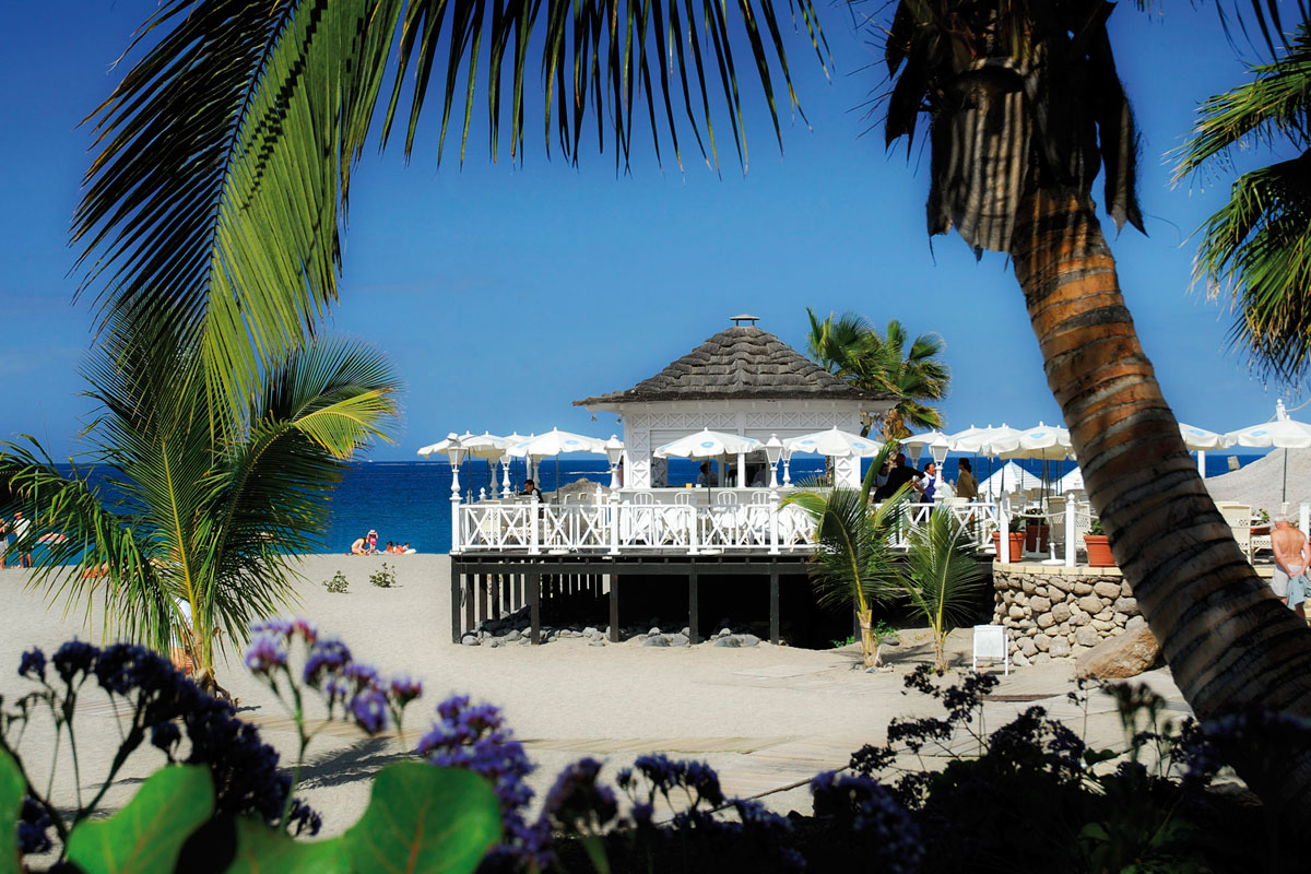 Weißer Kiosk am Strand mit Palmen und blauem Meer auf Teneriffa.