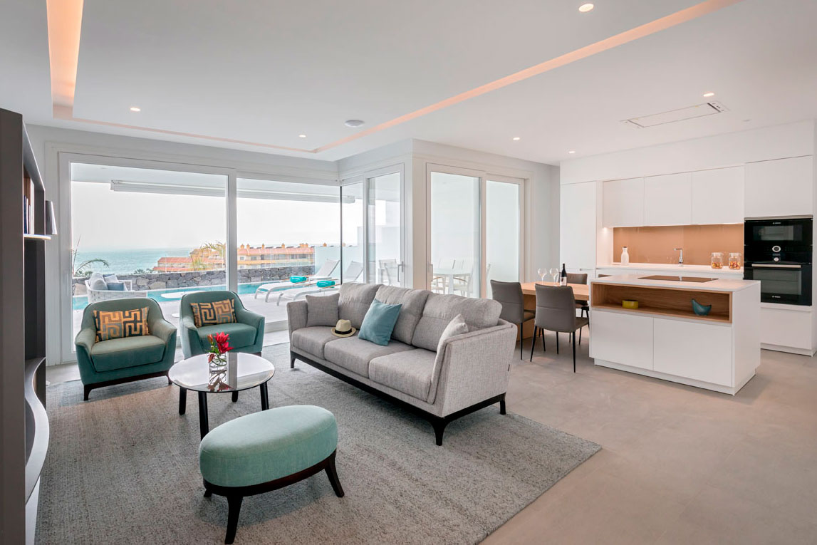 Modernes Wohnzimmer mit Meerblick auf Teneriffa, graue Sofas und integrierte Küche.