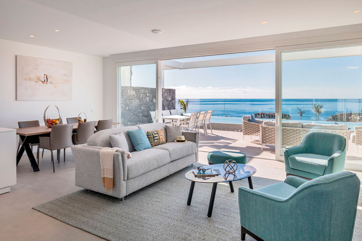 Modernes Wohnzimmer mit Meerblick auf Teneriffa. Graues Sofa, blaue Stühle und Tisch.