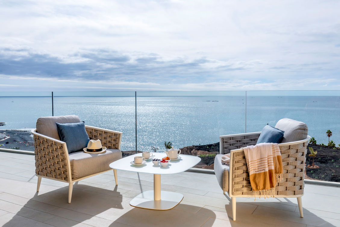 Terrasse mit Stühlen und Tisch zum Meer hin auf Teneriffa, blauer Hintergrund und bewölkter Himmel.