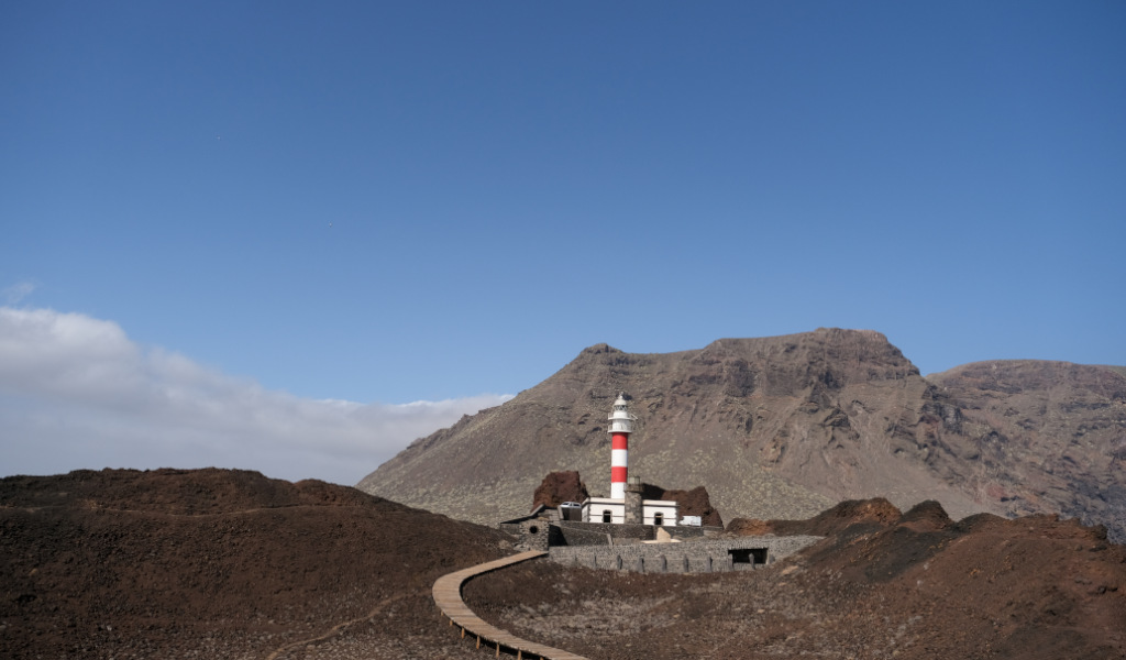 Leuchtturm in der Vulkanlandschaft von Punta de Teno, Teneriffa, vor Bergen und blauem Himmel.