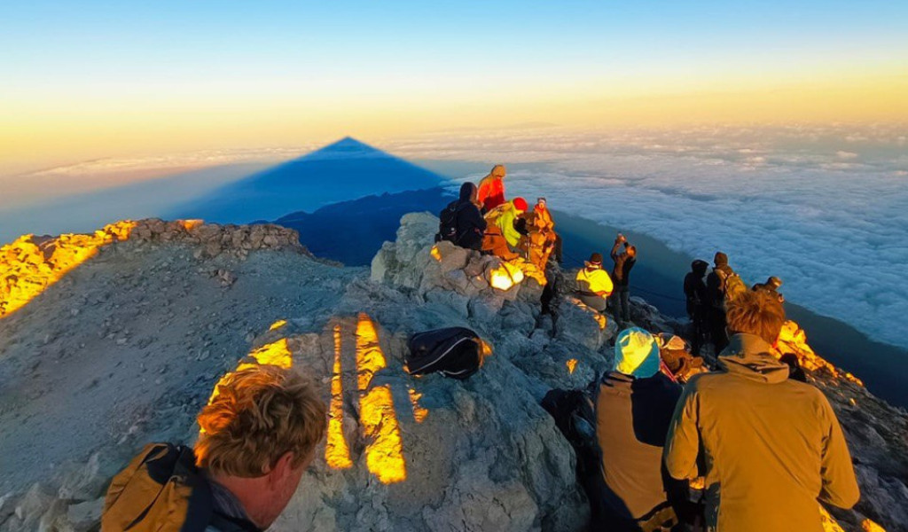 Besuchergruppe auf dem Gipfel des Teide bei Sonnenaufgang, mit Wolkenmeer im Hintergrund.