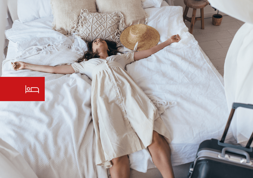 Person, die sich auf einem Bett neben einem Koffer und einem Hut auf Teneriffa ausruht.