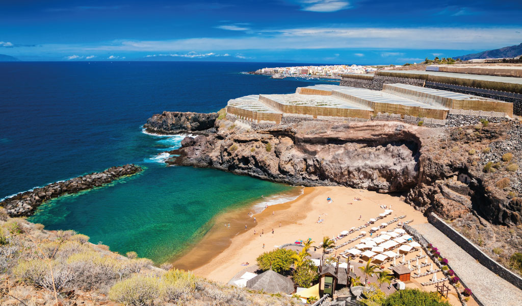 Strand mit Sonnenschirmen und blauem Meer in Puerto de Santiago, Teneriffa.
