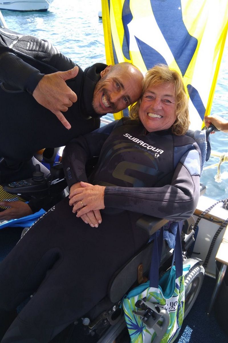 Menschen in lächelnden Tauchanzügen im Rollstuhl am Meer auf Teneriffa.