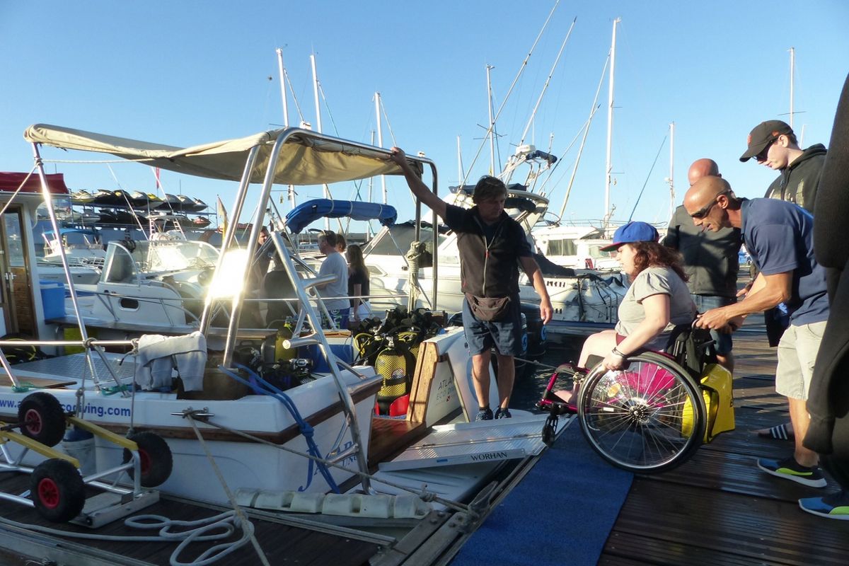 Person im Rollstuhl, die mit Hilfe mehrerer Personen auf Teneriffa ein Boot besteigt.