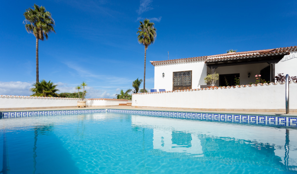 Schwimmbad und Haus mit Palmen auf Teneriffa unter blauem Himmel.