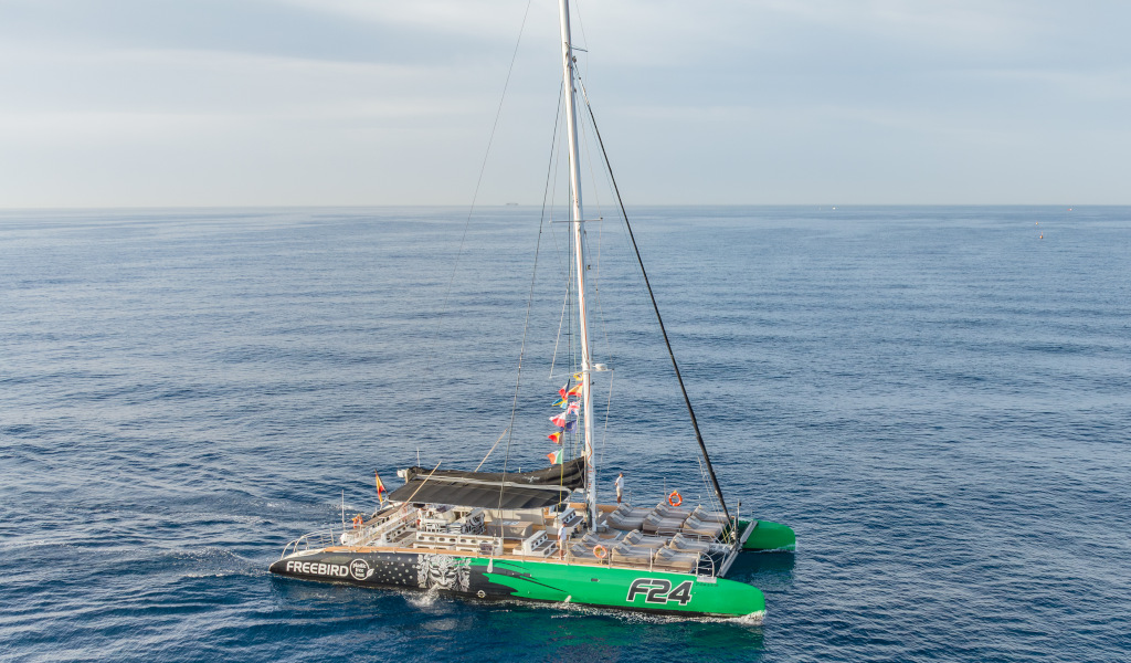Katamaran segelt auf dem Meer bei Teneriffa, mit Segeln und bunten Flaggen.