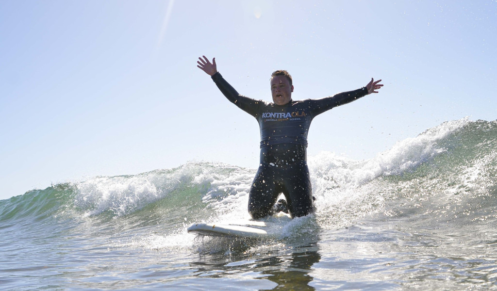 Surfer auf einer Welle mit ausgestreckten Armen, Kontraola-T-Shirt. Surfen auf Teneriffa.