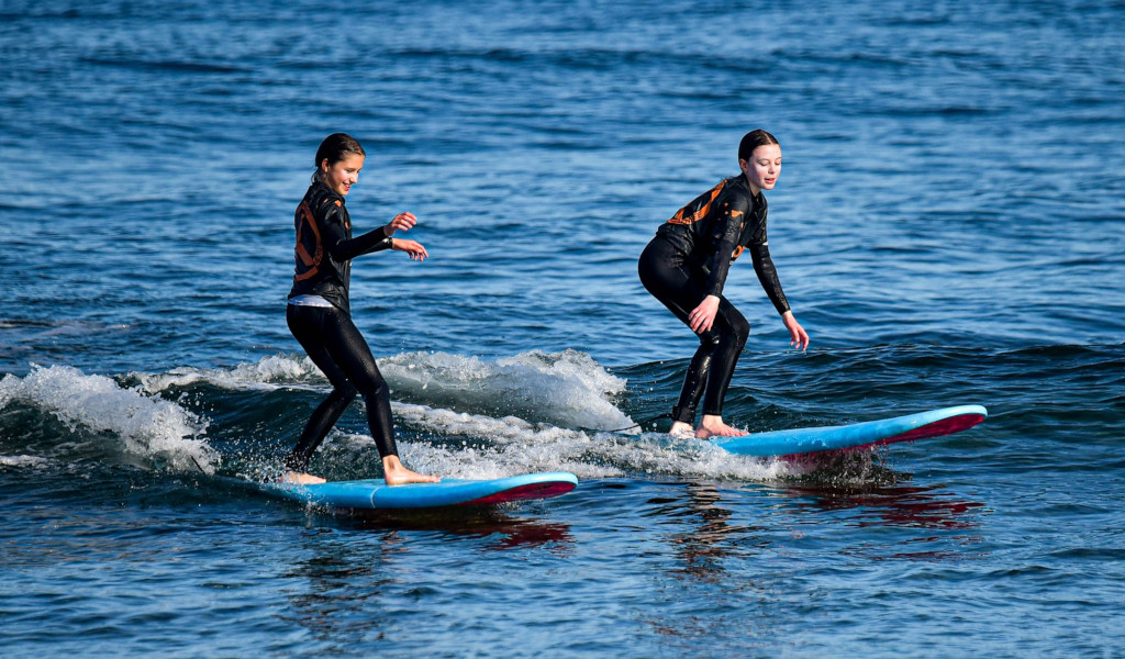 Zwei Personen in Neoprenanzügen surfen auf kleinen Wellen im Meer von Teneriffa.
