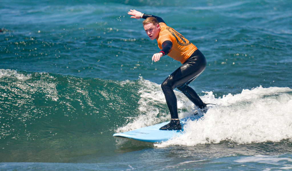 Person, die auf Teneriffa eine Welle surft und einen orangefarbenen Neoprenanzug trägt.