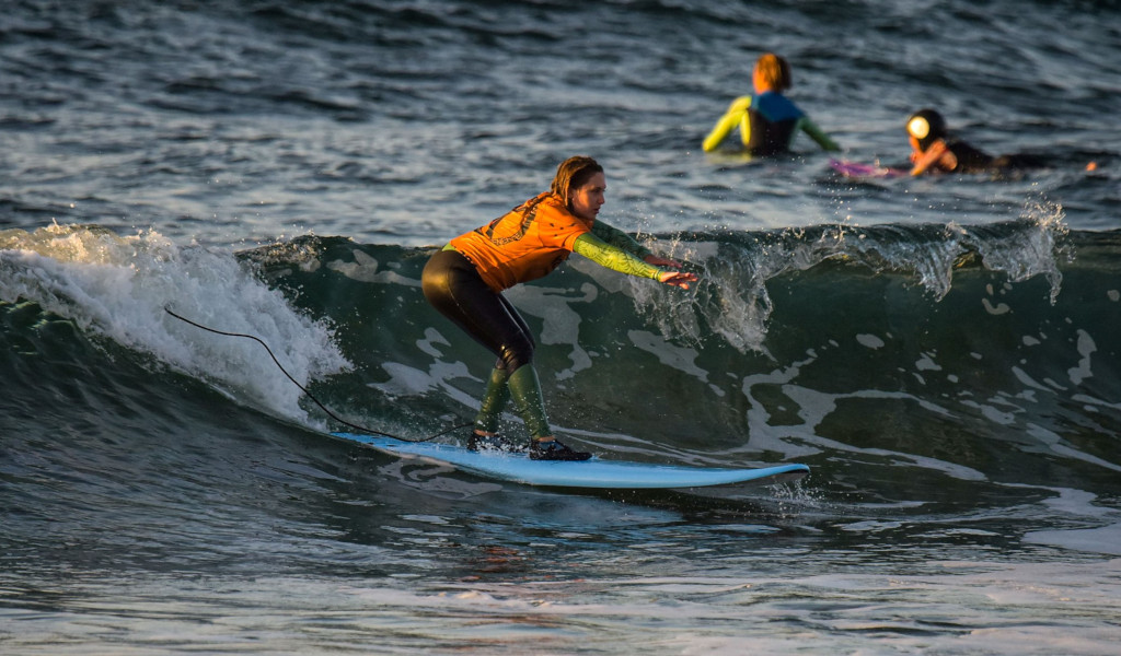 Surfer am Strand auf Teneriffa, der bei Sonnenuntergang auf einer Welle reitet.