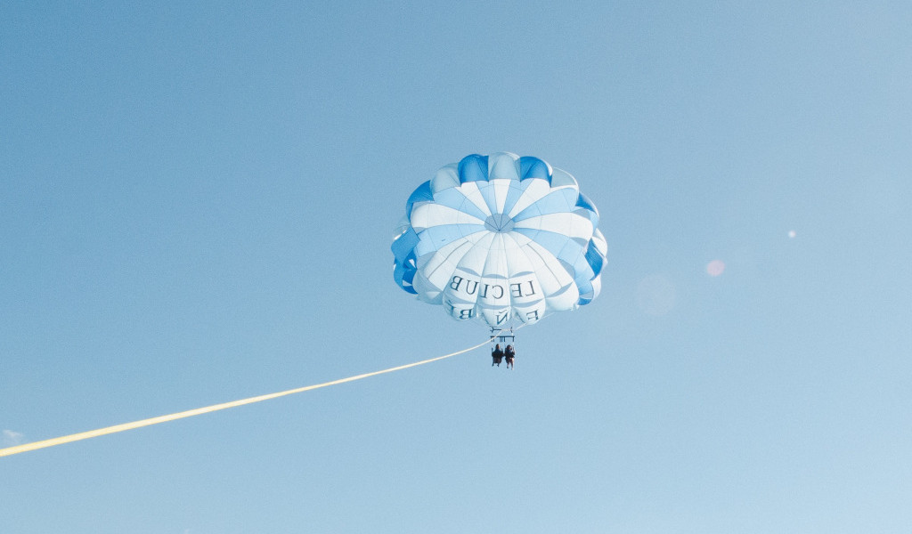Parasailing über den Himmel von Teneriffa mit Menschen unter weißen und blauen Fallschirmen.