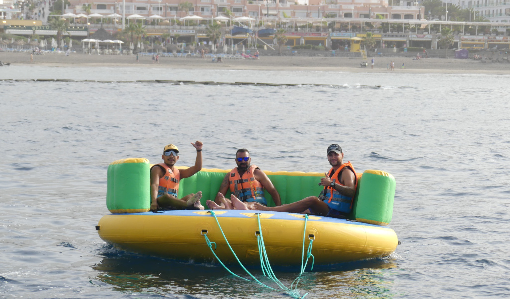 Drei Personen auf einer aufblasbaren Plattform im Meer, Playa de las Americas im Hintergrund, Teneriffa.