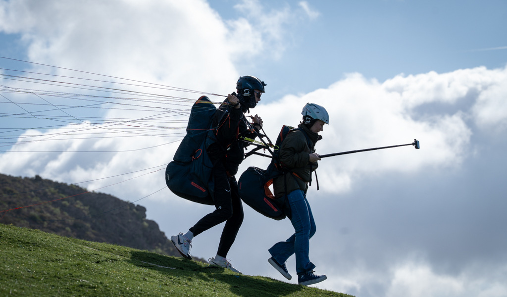 Zwei Personen starten beim Paragliding auf Teneriffa unter bewölktem Himmel.