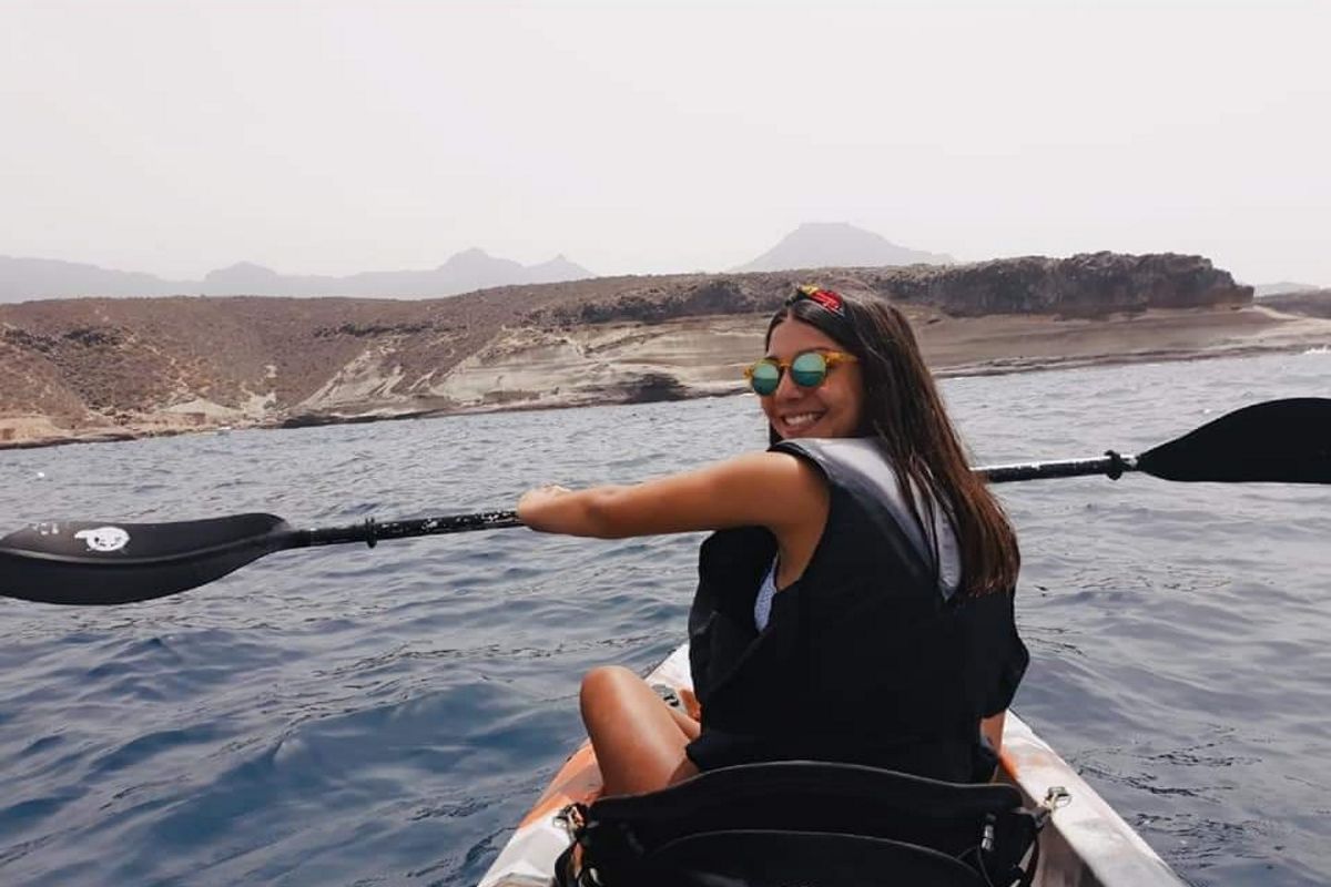 Person, die mit einem Kajak in den Gewässern von Teneriffa paddelt, mit bergiger Landschaft im Hintergrund.