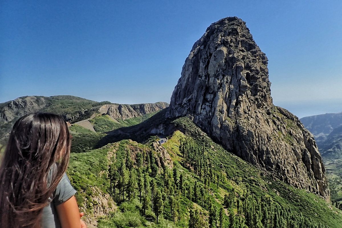 Frau, die den Roque de Agando auf Teneriffa beobachtet, umgeben von Vegetation.