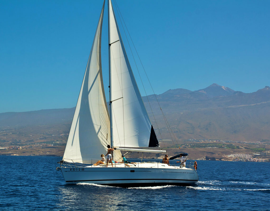 Segelboot segelt vor der Küste Teneriffas mit Bergen im Hintergrund.