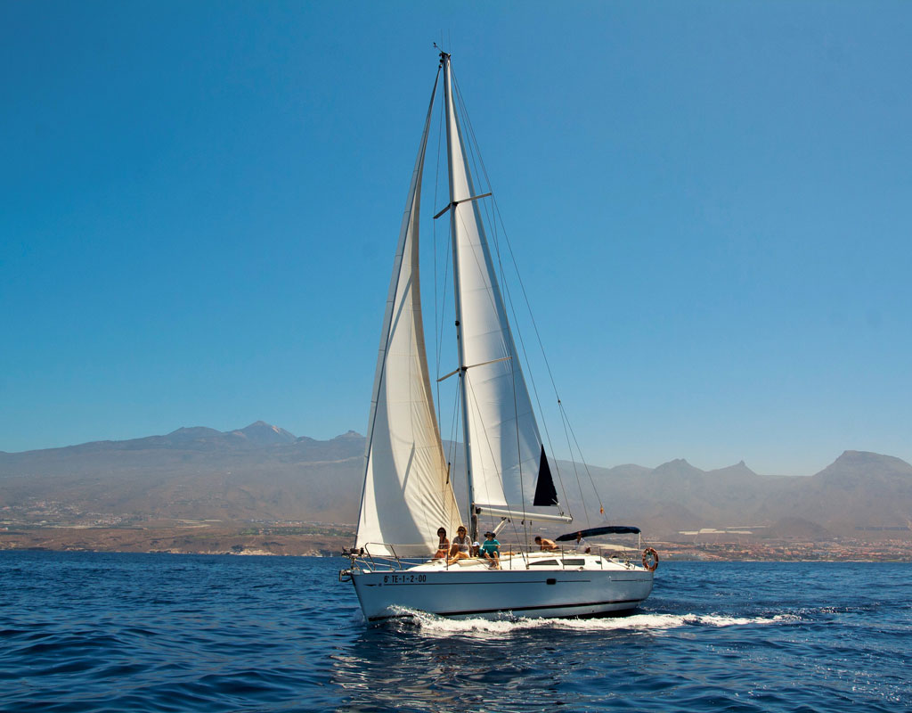 Segelboot segelt vor der Küste Teneriffas mit Bergen im Hintergrund.