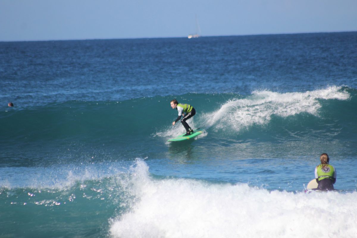 Surfer reitet auf einer Welle auf Teneriffa, während eine weitere Person vom Wasser aus zuschaut.