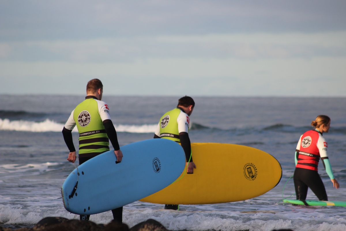 Surfer, die mit bunten Boards auf Teneriffa ins Meer eintauchen.