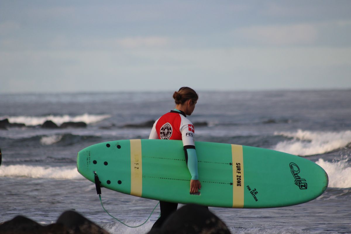 Person mit grünem Surfbrett am Strand auf Teneriffa