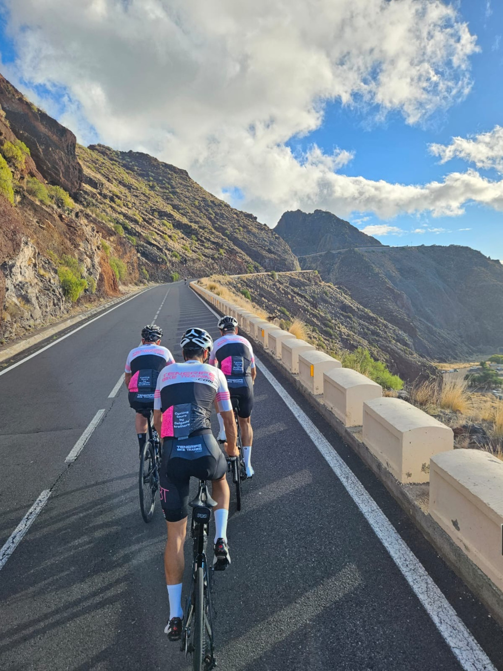 Radfahrer, die eine bergige Straße auf Teneriffa unter teilweise bewölktem Himmel erklimmen.