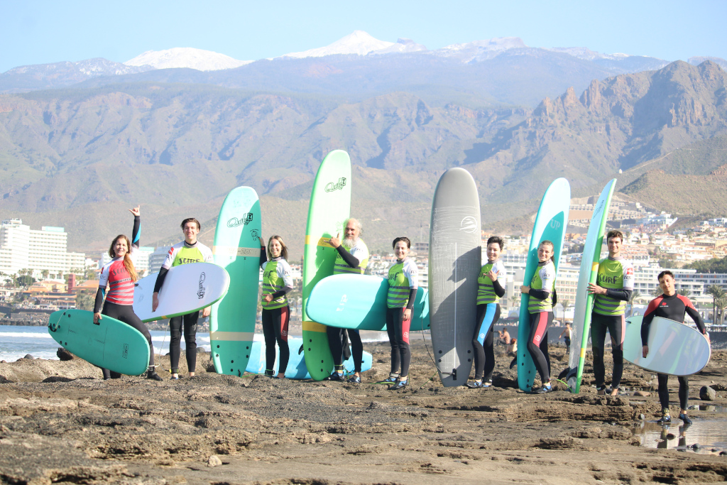 Eine Gruppe von Surfern mit Brettern am Strand von Teneriffa, Berge im Hintergrund.